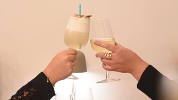 Dos manos sosteniendo copas de vino con una pajita, una mesa blanca y un vaso transparente.