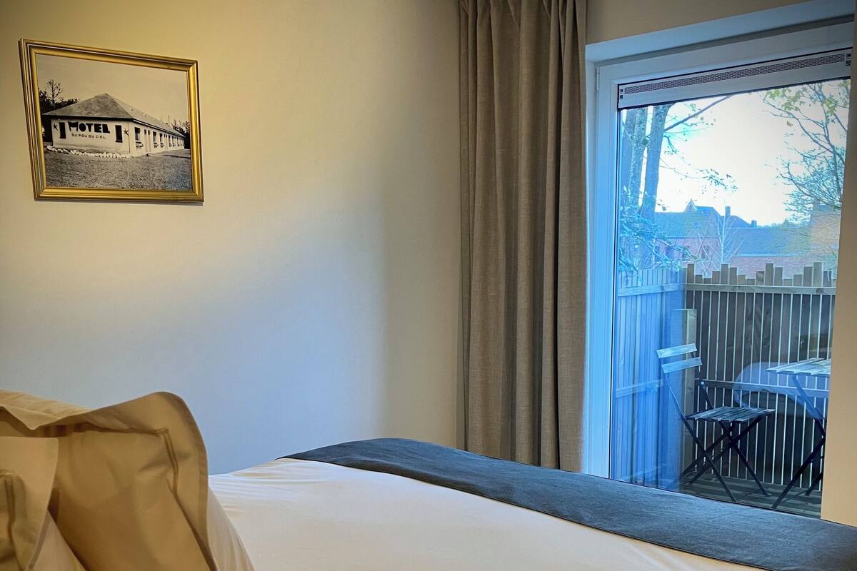 Hotellihuone, jossa on sänky, ikkuna, josta on näkymä ulos, seinällä oleva taulu ja verho.