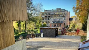 A paved courtyard with a small building, trees, and a multi-story residential building in the background. - Li Ter Hôtel&Restaurant (Marche-en-Famenne)