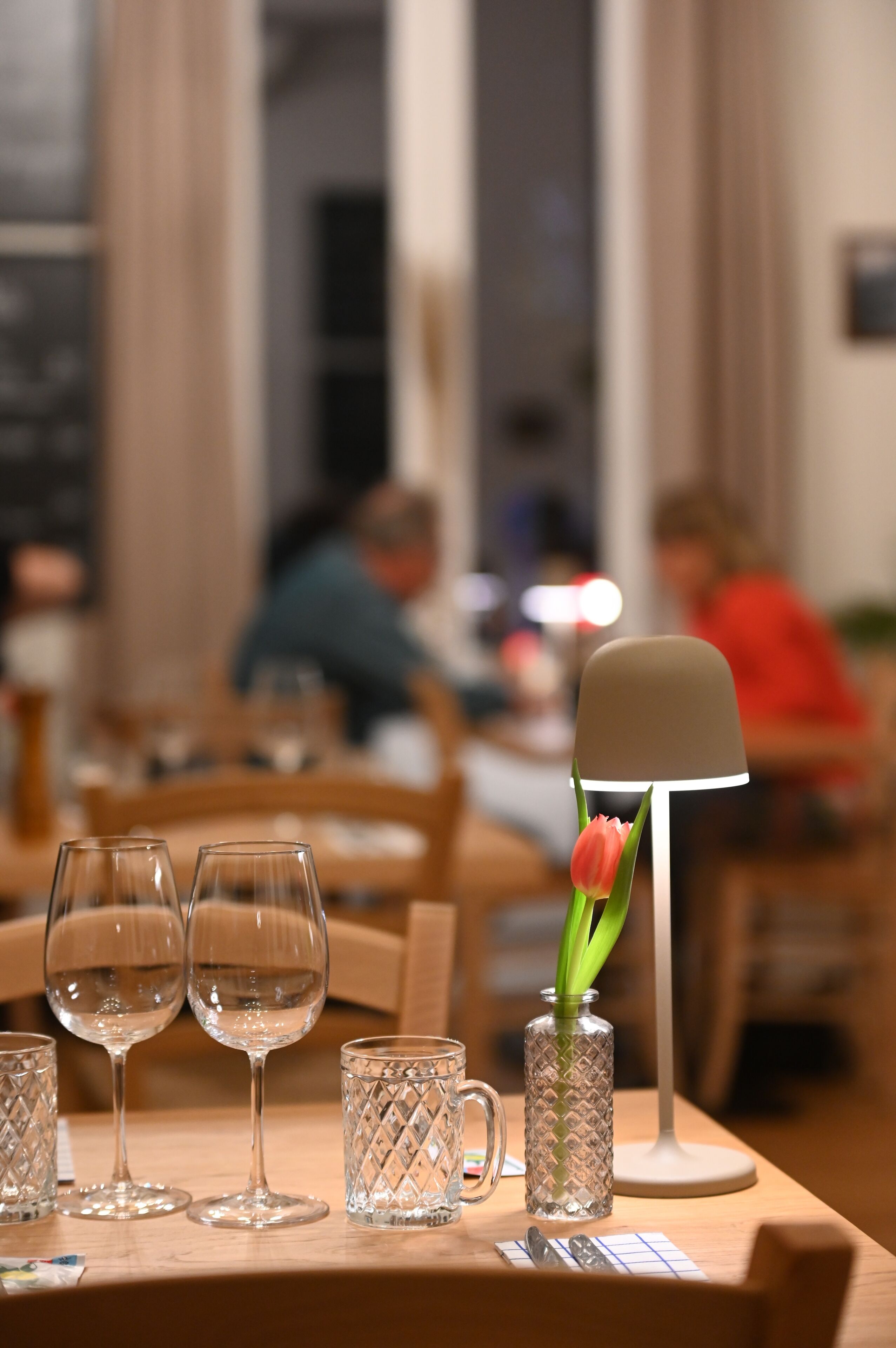 Una mesa de comedor con cristalería transparente y un florero con una sola tulipán.