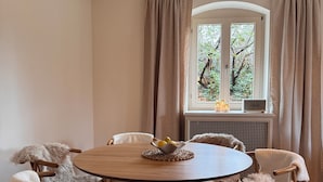 A dining area with a round wooden table, six chairs, and a window with curtains. - Family- & dog-friendly apartment near the Elbe with direct access to the park (Dresden)
