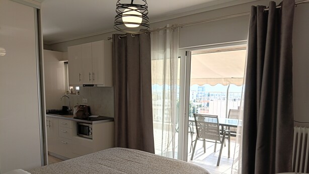 Quarto com cama, uma pequena cozinha e varanda com mesa e cadeiras.