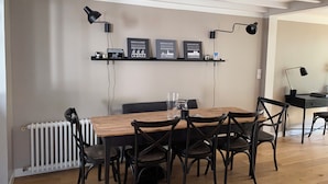 Uma sala de jantar com mesa de madeira e cadeiras pretas, um radiador branco e luminárias pretas fixadas na parede.