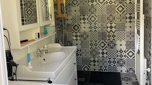 Casa de banho com lavatório branco, espelho e área de duche.