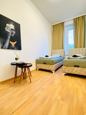 A room with two beds, a small table with a vase, and a painting on the wall. - 5 Bedroom Apartment near Schonbrunn (Vienna)