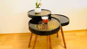 A room with a large black and white artwork on the wall, a small white vase with a single white flower, and two black tables with gold designs. - 5 Bedroom Apartment near Schonbrunn (Vienna)