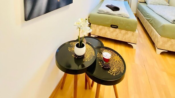 A modern bedroom with two single beds, a large abstract painting, a small round table with a vase of flowers, and a view of a building through the window. - 5 Bedroom Apartment near Schonbrunn (Vienna)