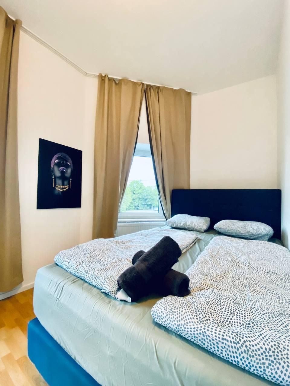 A bedroom with a bed, beige curtains, a window, and a framed picture on the wall.