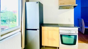 A compact kitchen with a refrigerator, oven, and a small cabinet. A window provides natural light, and a door leads to another room. - Budget Friendly 4 BR Apt for Groups (Vienna)
