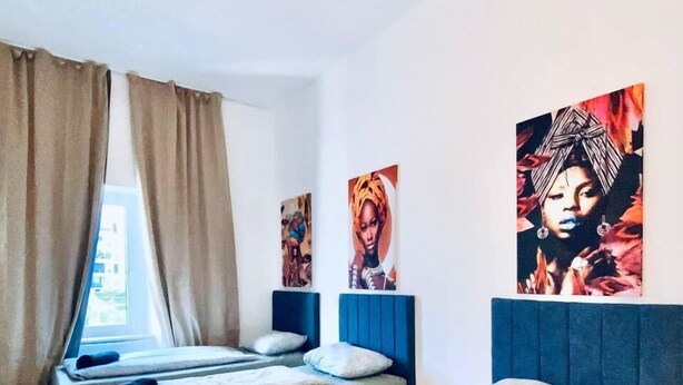 A room with two beds, beige curtains, and artwork on the walls. - Budget Friendly 4 BR Apt for Groups (Vienna)