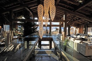 Ruime binnenruimte met een hoge plafond, houten balken en een centrale trap. Er zijn zitgedeeltes met banken en een glazen balustrade.