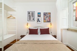 A bedroom with a bed, two bedside tables, a wardrobe, and three framed artworks on the wall.
