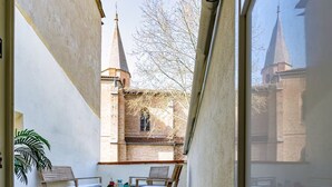A balcony with two wooden chairs and a small table, overlooking a church with a tall spire. - House T3 Gaillac Centre-Cosy-Netflix-Parking (Gaillac)