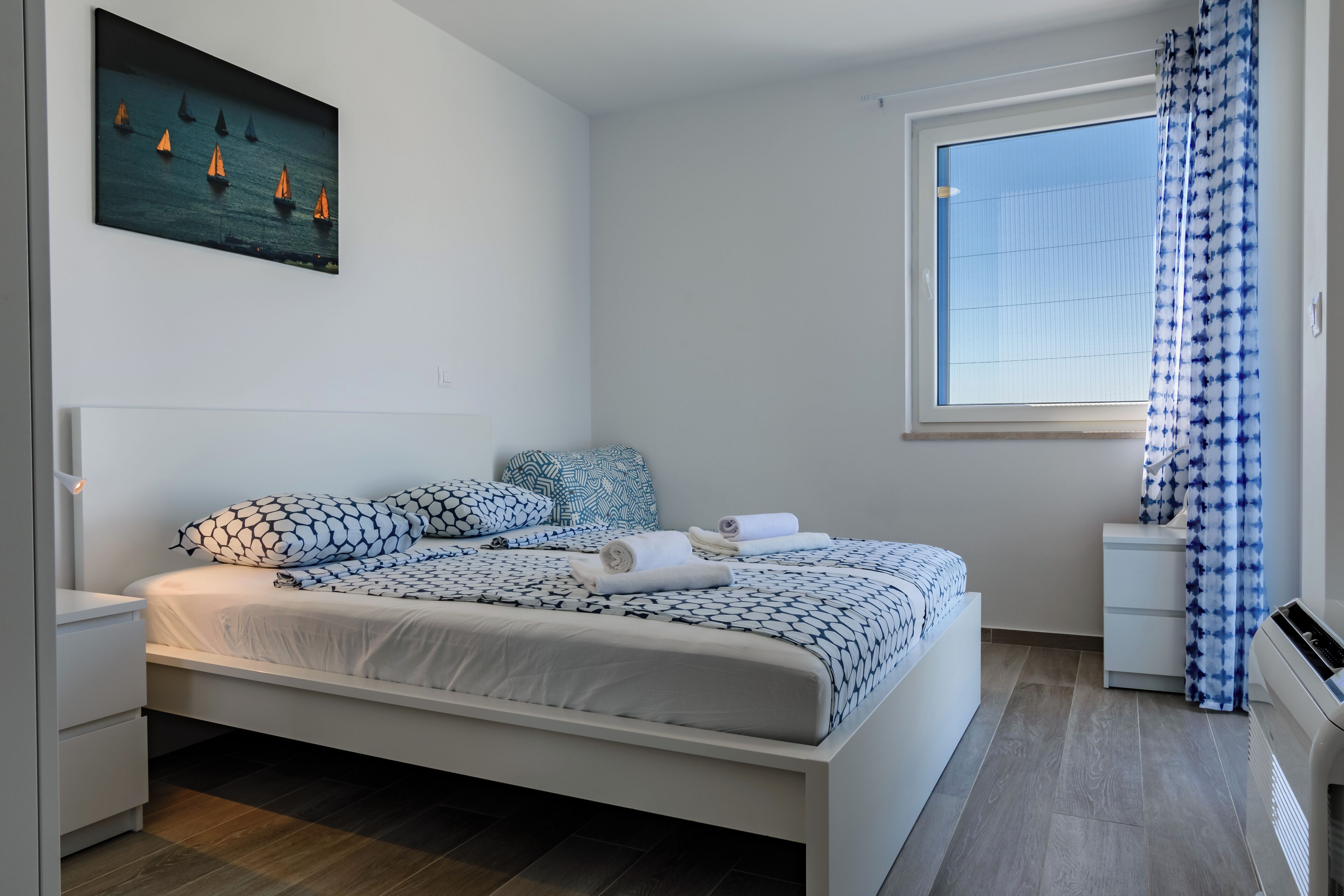 Een moderne slaapkamer met een bed, nachtkastjes, een schilderij en een raam met gordijnen.