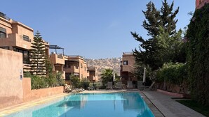 Ein Swimmingpool mit gefliesten Rändern, umgeben von Gebäuden mit Balkonen und Bepflanzung.