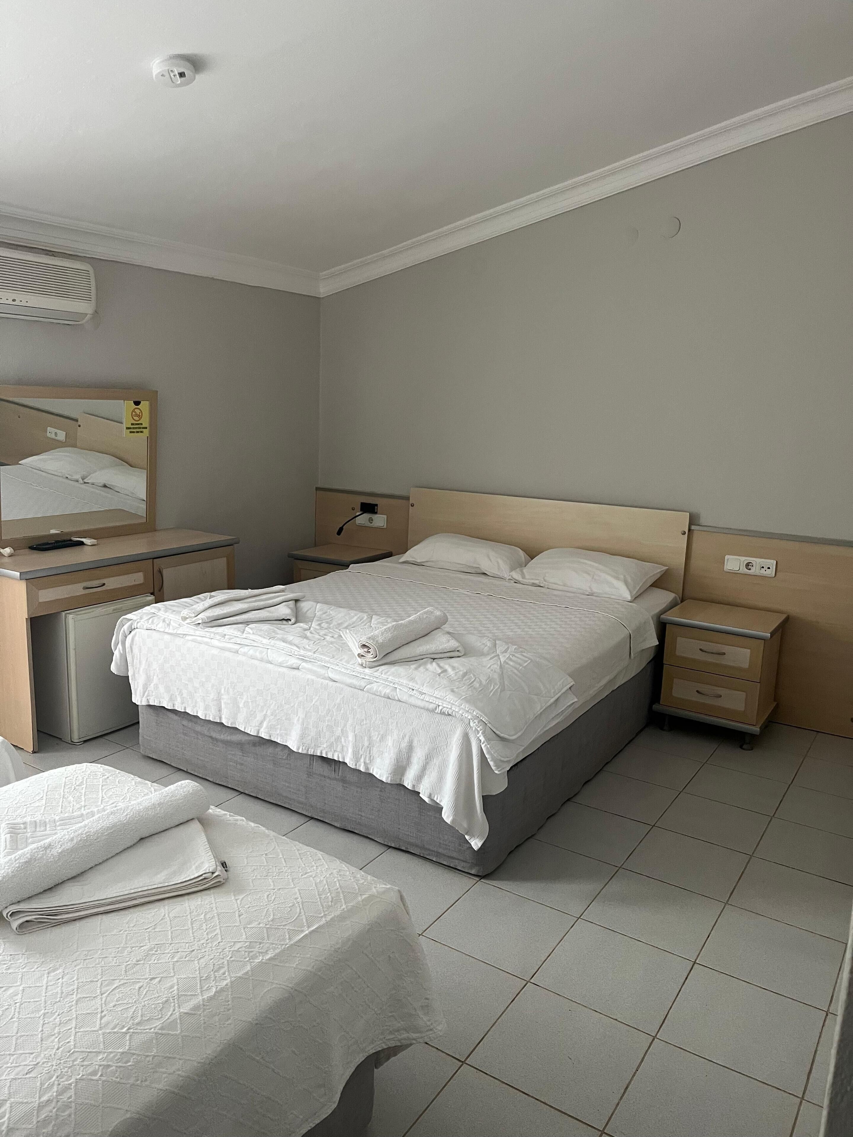 A hotel room with a bed, bedside tables, a desk, a chair, and a mirror.