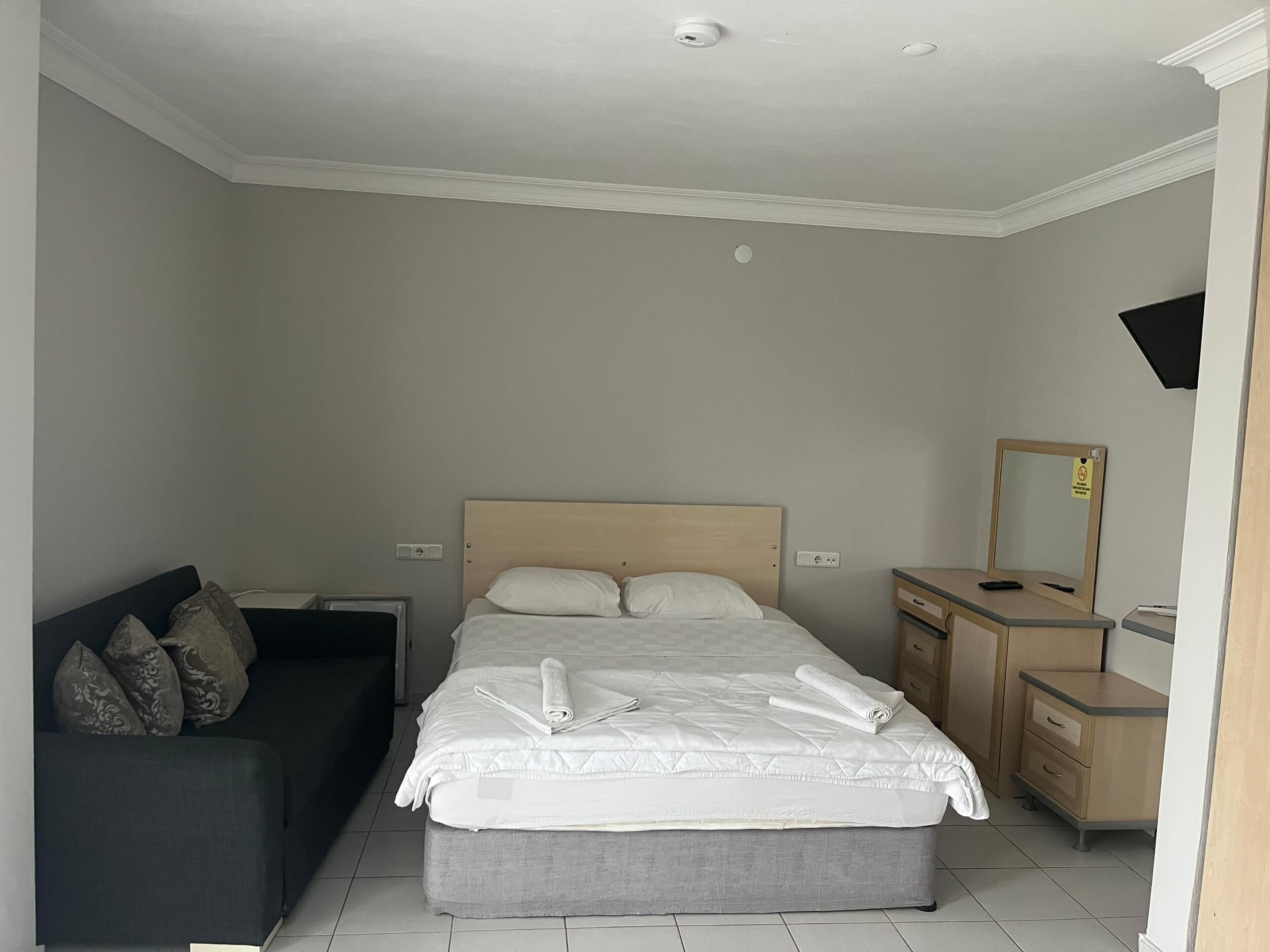 A hotel room with a bed, a bedside table, a dresser, a mirror, and a sofa.