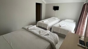 A hotel room with two single beds, a desk with a chair, a flat-screen TV mounted on the wall, and a door leading to another room. - Eldorado Hotel (Kumluca)