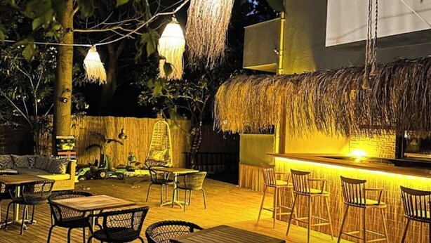 An outdoor seating area with wooden tables and chairs, hanging lights, and a thatched roof bar. - Eldorado Hotel (Kumluca)