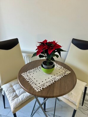 A round wooden table with a green pot and red poinsettia plant, surrounded by two chairs with white cushions.