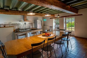 A spacious kitchen with a large wooden table, modern appliances, and a view of greenery outside.