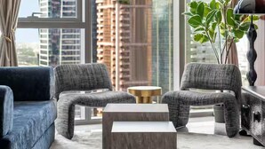 A modern living room with a large window, a blue sofa, two grey armchairs, a marble coffee table, and a hanging light fixture. - Paramount Hotel Rooftop Infinity Pool (Dubai)