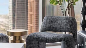 A modern living room with a gray sofa, a small side table, and a potted plant. A large window offers a view of tall buildings. - Paramount Hotel Rooftop Infinity Pool (Dubai)