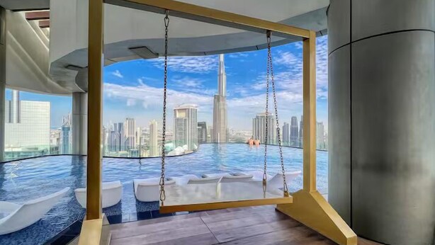 A modern room with a swing chair overlooking a cityscape and a pool. - Paramount Hotel Rooftop Infinity Pool (Dubai)