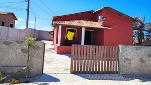 Una casa roja con techo de tejas, un portón de madera y un pequeño balcón con un paño amarillo.