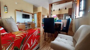 Un espacio habitable compacto con sofá, una mesa de comedor con sillas, televisor y zona de cocina.