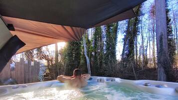 A hot tub in a forested area with a wooden deck and a canopy overhead.