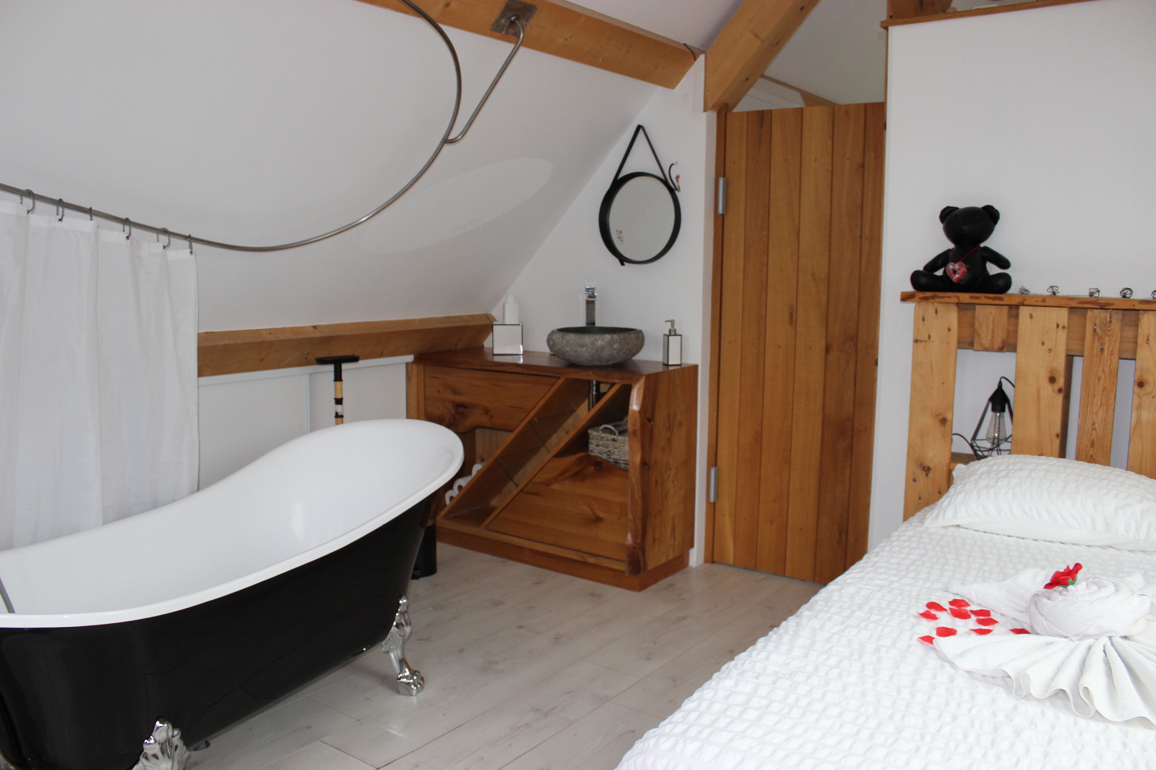 Een slaapkamer met een bed, een badkuip en een houten plankje met een teddybeer.