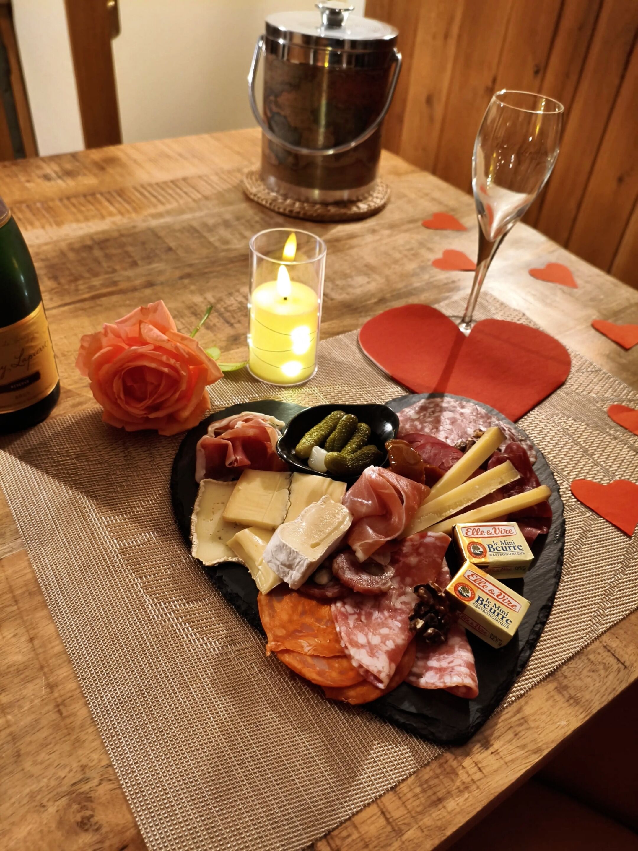 Uma tábua de frios com diversos queijos, carnes e picles sobre uma mesa de madeira.