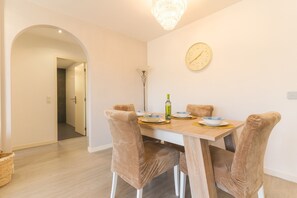 A dining area with a wooden table, four cushioned chairs, a chandelier, and a wall clock. - Sol Garajau Apartment by Atlantic Holiday (Santa Cruz)