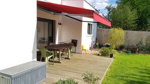 Een overdekt terras met een tafel en stoelen, een klein tuintje en een houten terras.
