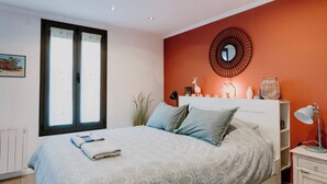 Een slaapkamer met een bed, nachtkastje, wandklok en raam.