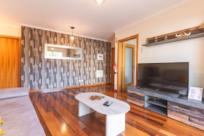 A modern living room with a flat-screen TV, a coffee table, and a patterned wall. - Judite Home Apartment by Atlantic Holiday (Santa Cruz)