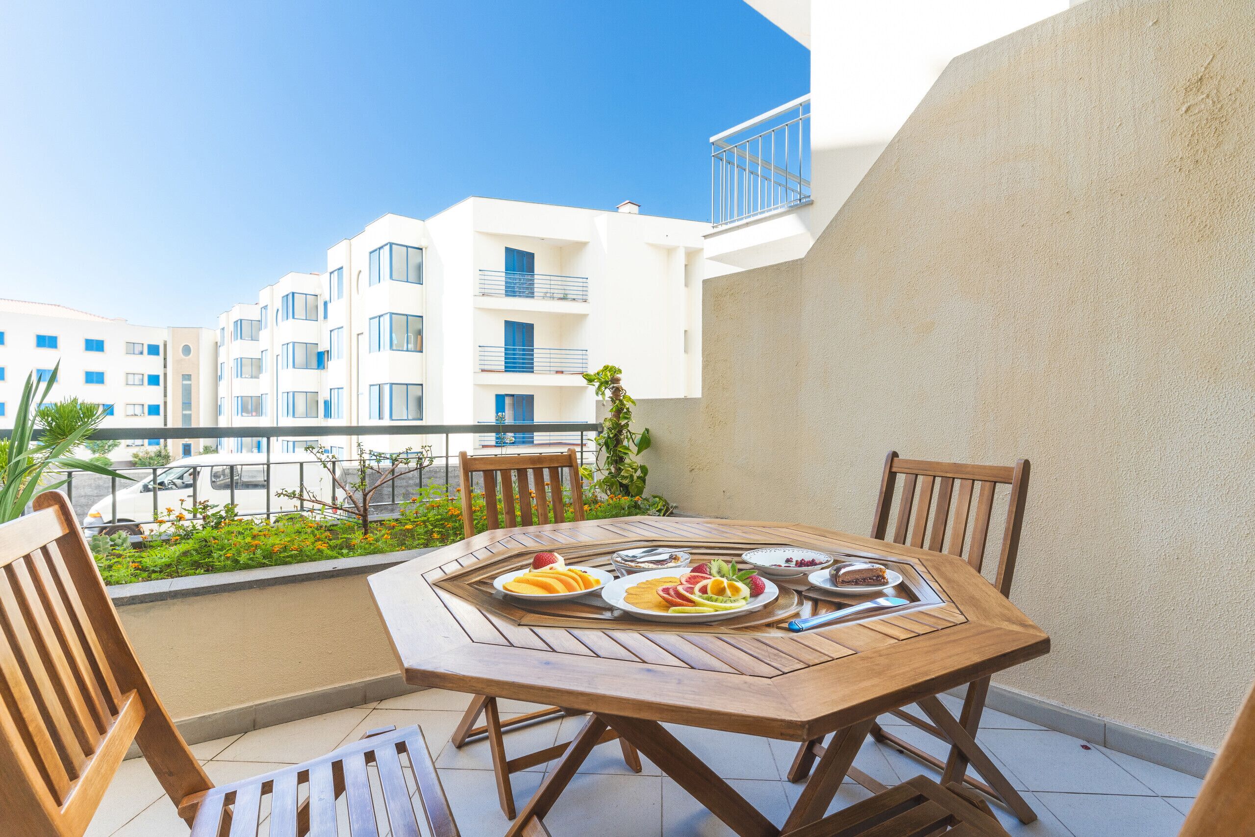 A wooden table with chairs on a balcony with a view of a white building with balconies.