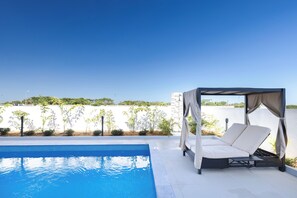 Zona junto a la piscina con una sombrilla y una silla reclinable.