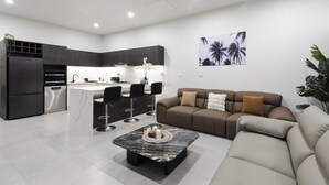 A modern kitchen with dark cabinetry, a central island, and bar stools. There is a living area with a sofa and a coffee table. - Cozy 2-bedroom apartment in adorable Wailoaloa Beach (Nadi)