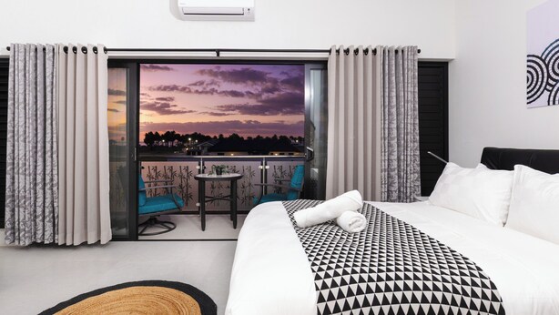 A hotel room with a large bed, a balcony with a view of the sunset, and a small table with chairs. - Cozy 2-bedroom apartment in adorable Wailoaloa Beach (Nadi)