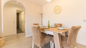 A dining area with a wooden table, four cushioned chairs, a chandelier, and a wall clock. - Sol Garajau Apartment by Atlantic Holiday (Santa Cruz)