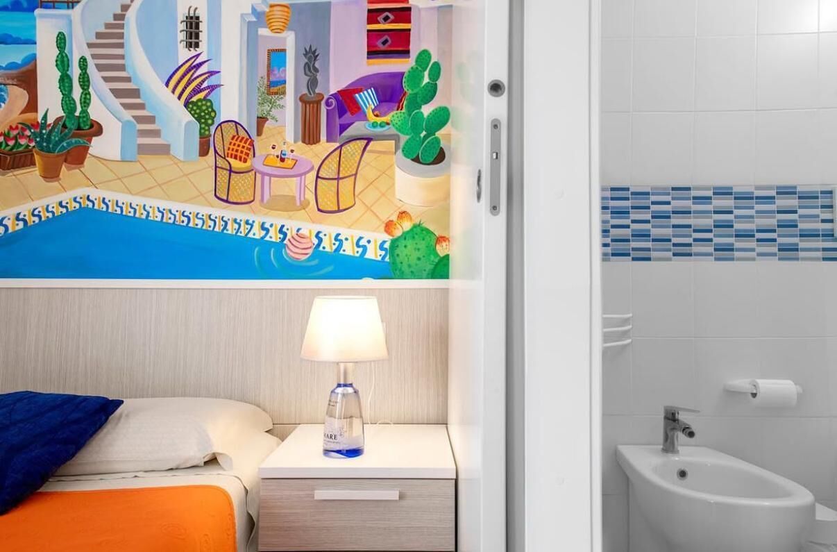 Una habitación de hotel con cama, mesita de noche, lámpara y baño con bidé.