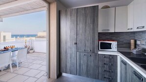A modern kitchen with grey cabinets, a microwave, and a dining area with a table and chairs. - La Terrazza sul Porto B&B (San Foca)