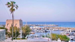 A coastal marina with boats docked, a palm tree, and a building with a unique architectural style. - La Terrazza sul Porto B&B (San Foca)