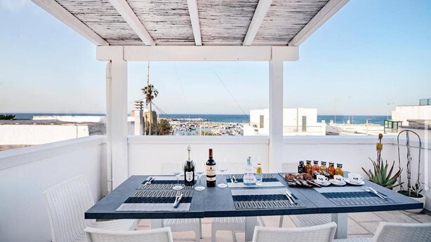 A rooftop terrace with a table set for dining, overlooking a coastal cityscape. - La Terrazza sul Porto B&B (San Foca)