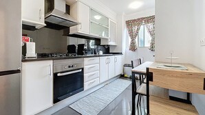 A compact kitchen with white cabinets, a stove, and a dining area with a table and chairs. - Judite Home Apartment by Atlantic Holiday (Santa Cruz)