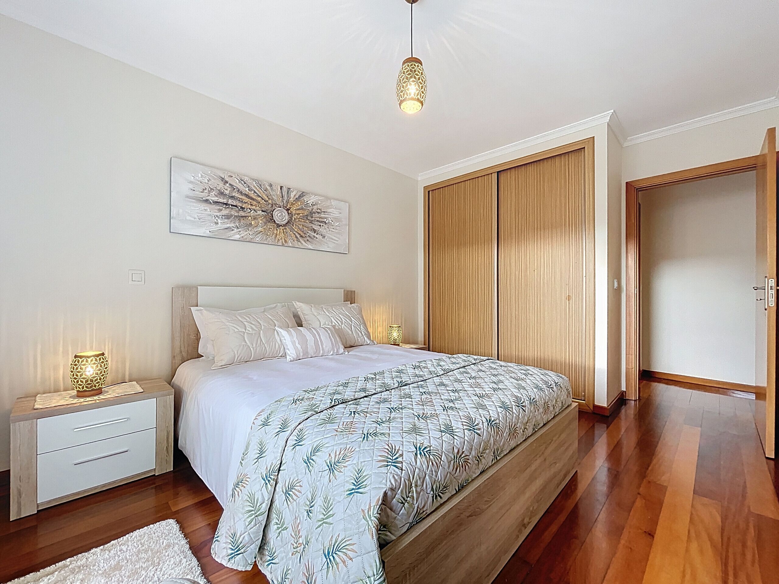 A bedroom with a bed, nightstands, a bedside lamp, a wall art piece, and a wardrobe.