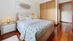 A bedroom with a bed, nightstands, a bedside lamp, a wall art piece, and a wardrobe. - Judite Home Apartment by Atlantic Holiday (Santa Cruz)