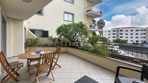 A balcony with a wooden table and chairs, surrounded by potted plants and flowers. - Judite Home Apartment by Atlantic Holiday (Santa Cruz)